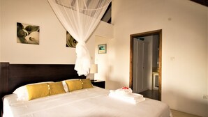 A neatly made bed with white and yellow bedding, a bedside table with a lamp, and artwork on the walls. - Apartment La Batie self catering for 2 on Beau Vallon (Mahe)