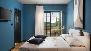 A bedroom with a large bed, a TV mounted on the wall, and a view of the outdoors through a glass door.