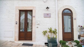 Un edificio blanco con dos puertas de madera, un letrero sobre la puerta derecha y macetas con plantas afuera.