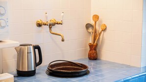 Una cocina con encimera de azulejos azules, un hervidor de acero inoxidable, un grifo de latón y utensilios de madera en un jarrón.