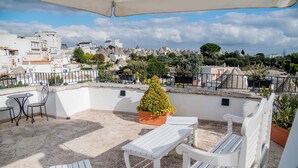 Terraza en la azotea con mobiliario blanco, una planta en maceta y vistas a un pueblo con edificios blancos.