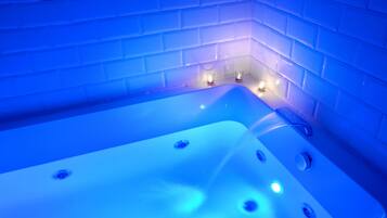 A modern bathroom with a large bathtub, blue lighting, and two lit candles on the wall.