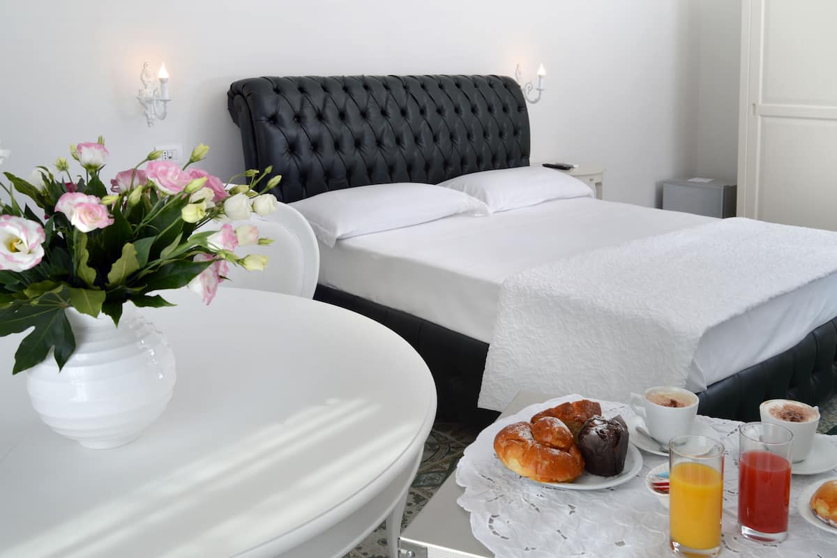 A hotel room with a bed, a bedside table with breakfast items, and a vase of flowers.