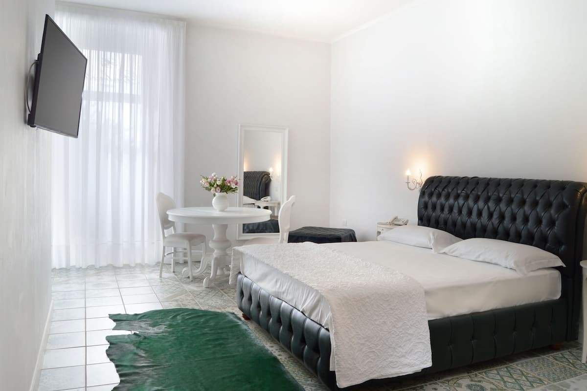 A hotel room with a bed, a desk, a chair, a TV, and a mirror.