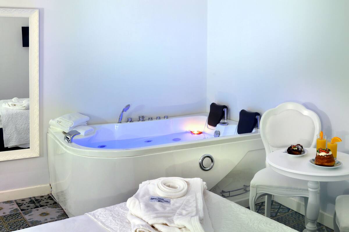 A bathroom with a bathtub, a mirror, a towel rack, a sink, and a small table with a drink and a dessert.