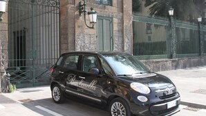 A black compact car parked in front of a historic building with ornate iron gates and green shutters. - Barbarella Home (Naples)