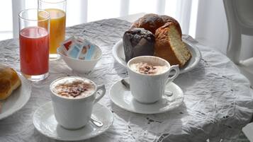 Una mesa con mantel de encaje blanco, dos tazas de café, una hogaza de pan y dos vasos de jugo.