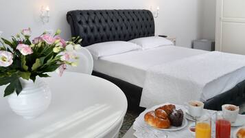 A hotel room with a large bed, a bedside table with breakfast items, and a vase of flowers.