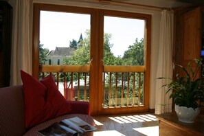Una stanza con un balcone in legno, un divano con cuscini rossi e una pianta in vaso.