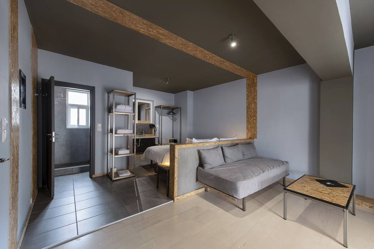 A modern, well-lit room with a grey sofa, a small wooden table, and a built-in shelving unit with a mirror.