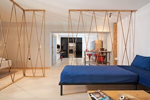 Un dormitorio moderno con cama azul, suelo de madera y una zona de cocina al fondo.