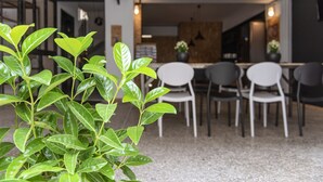 A modern dining area with a kitchen in the background, featuring a dining table with chairs and a potted plant in the foreground. - Piraeus Premium Suites (Piraeus)