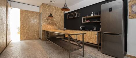 A modern kitchen with a wooden table, hanging pendant lights, a stainless steel refrigerator, and built-in shelves.