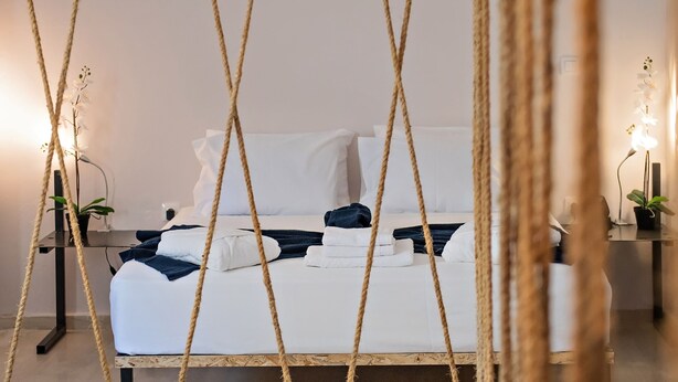 A modern bedroom with a bed framed by rope, white bedding, and two bedside tables with lamps. - Piraeus Premium Suites (Piraeus)