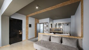 A modern living room with a grey sofa, wooden beams, a black door, and a kitchen area with a countertop and cabinets. - Piraeus Premium Suites (Piraeus)