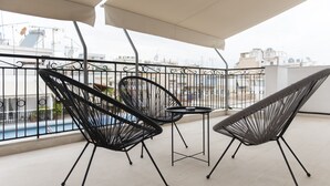 A balcony with two black wireframe chairs and a small table, overlooking a cityscape with buildings and a pool. - Piraeus Premium Suites (Piraeus)