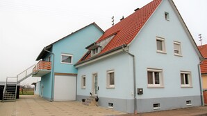 Ein zweistöckiges Haus mit rotem Dach, blauer Fassade und weißer Garagentür.