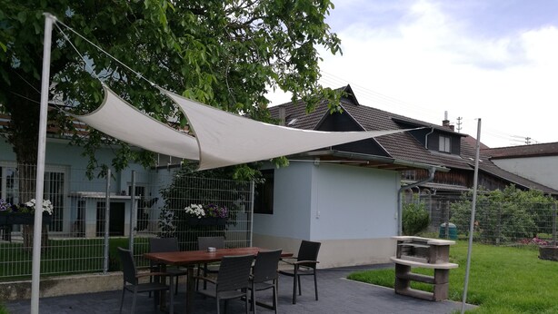 Eine Terrassenausstattung mit Tisch, Stühlen, einem Grill und einem weißen Sonnensegel.