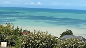 A coastal view with clear turquoise waters, a distant shoreline, and lush greenery in the foreground. - Vacation home "Bord de Mer" - Exceptional sea view (Petit-Caux)