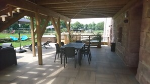 Eine Terrasse im Freien mit Tisch und Stühlen, umgeben von Steinmauern und einer Holzbalkendecke.