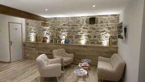 Une pièce avec un mur en pierre, deux fauteuils, une petite table et une étagère contenant des livres et des objets décoratifs.