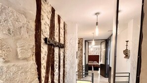 Un couloir aux murs en briques apparentes, une porte en bois et un escalier menant à une chambre.
