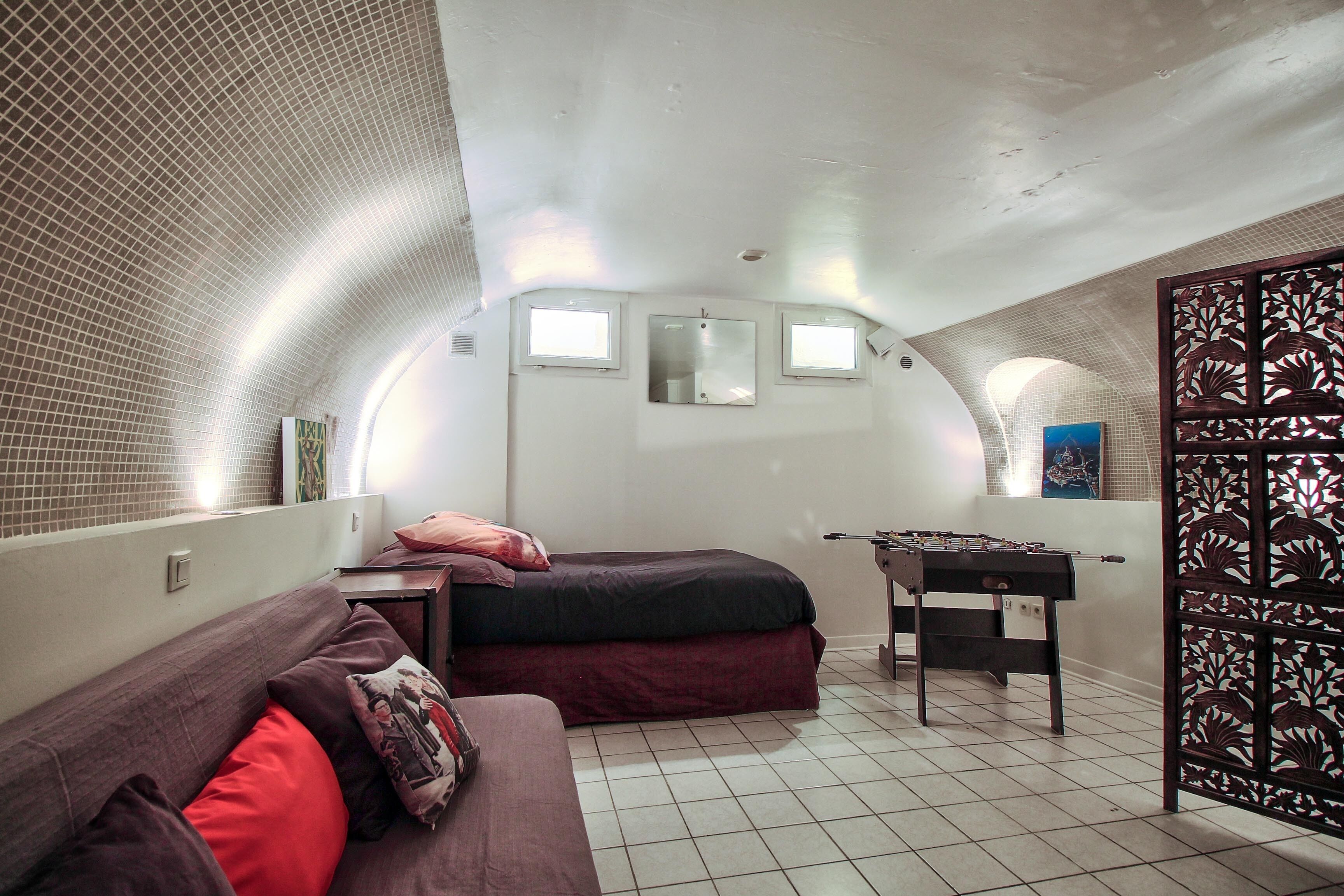 A compact room with a bed, a sofa, a foosball table, and a decorative partition.