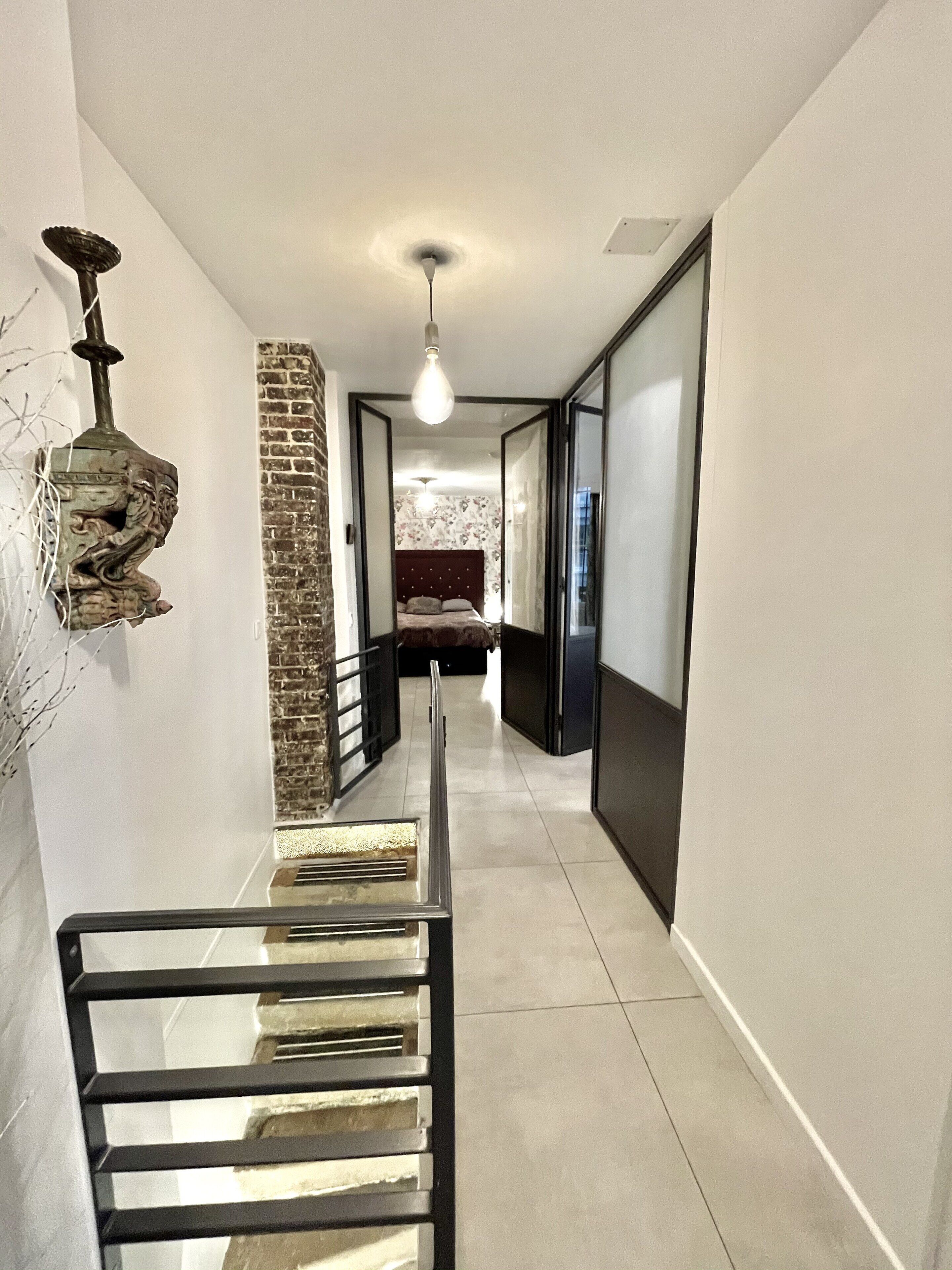 A modern hallway with a glass table, a brick accent wall, and a bed in the background.