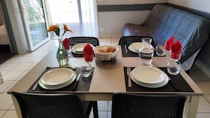 Un coin repas avec une table dressée pour deux personnes, comprenant des assiettes, des couverts, un vase avec des fleurs et une carafe d’eau.