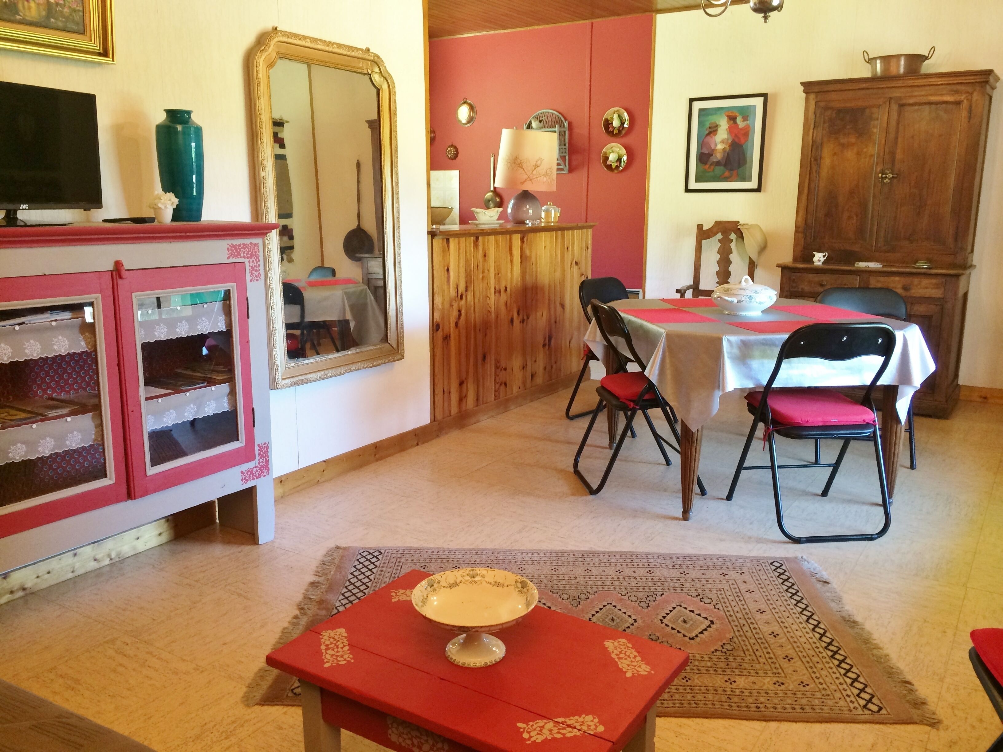 A dining area with a table set for two, a wooden cabinet, and a television on a stand.