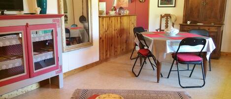 A dining area with a table set for two, a wooden cabinet, and a television on a stand.