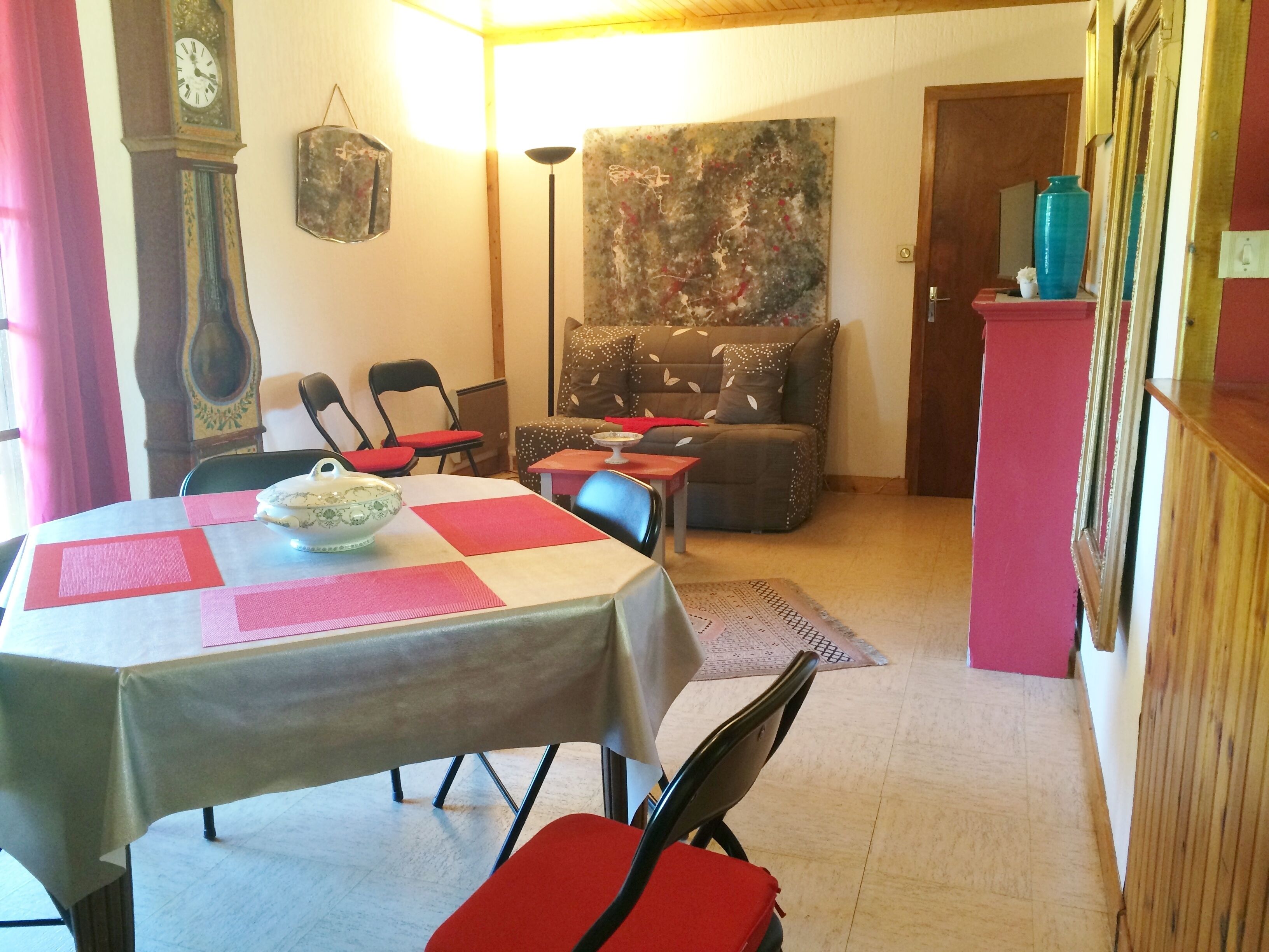 Un coin repas avec une table dressée pour deux personnes, des chaises, une horloge et un tableau accroché au mur.