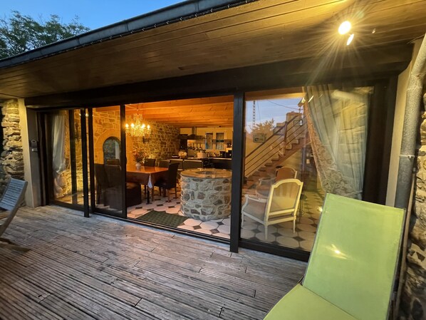A modern house with a stone exterior, a wooden deck, and a glass-enclosed dining area with a stone table and chairs.