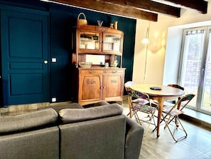 A cozy living room with a dark blue door, a wooden cabinet with glass doors, a round wooden table, and a gray sofa.