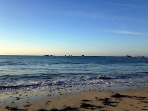 Ein Strand mit ruhigem Wasser, fernen Felsformationen und einem klaren Himmel.