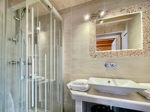 Ein modernes Badezimmer mit einer Duschkabine aus Glas, einem weißen Waschbecken mit einem Kieselmoos-Umrandung und einem Spiegel mit Holzrahmen.