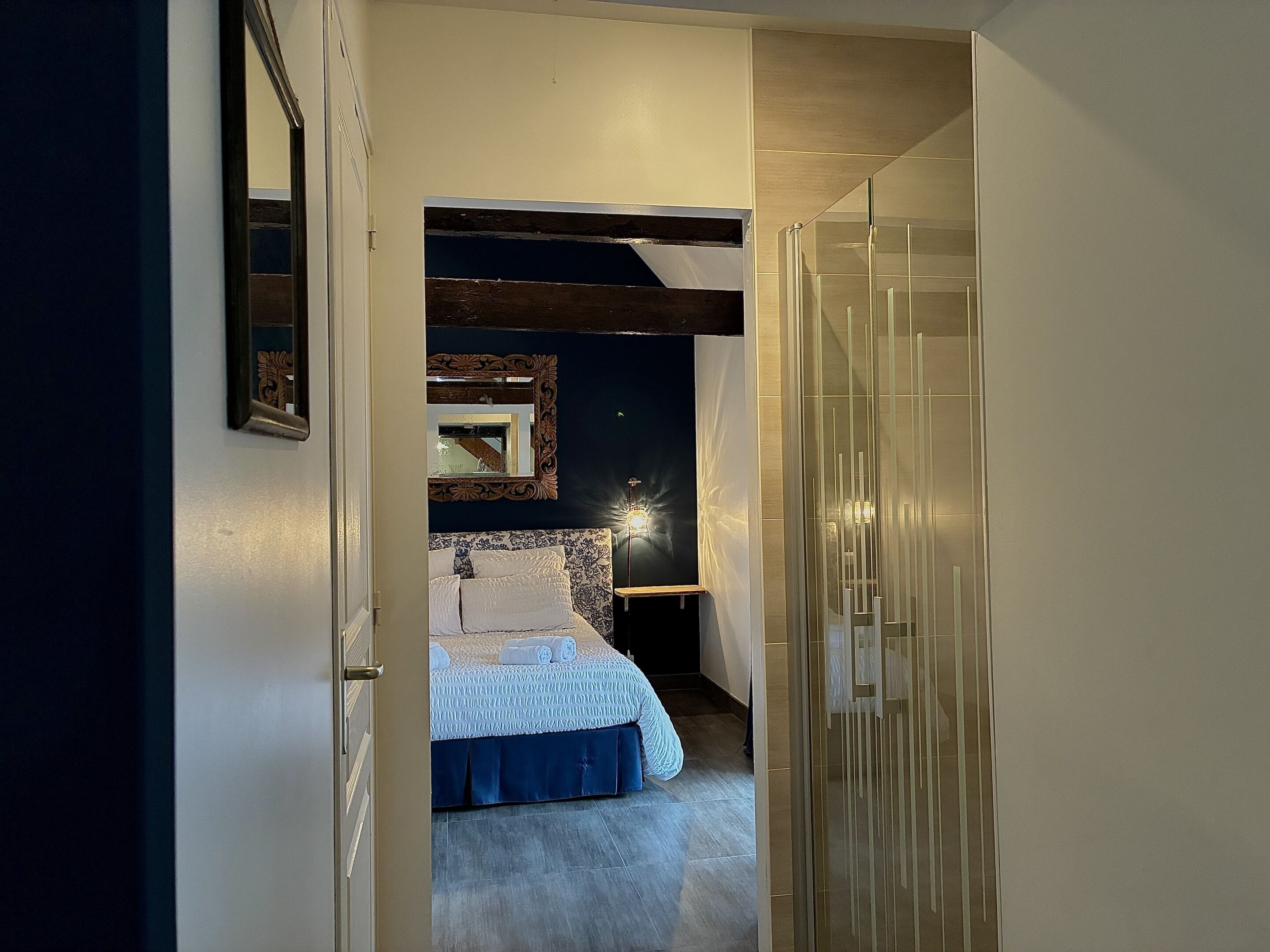 Un pasillo estrecho que conduce a un dormitorio con una cama, un espejo y una mesita de noche.