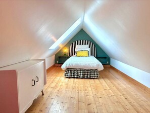 A bedroom with a sloped ceiling, a bed with a striped headboard, a checkered skirt, and a nightstand with a lamp.
