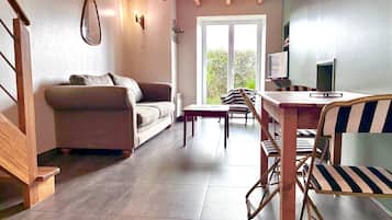 Un salon moderne comprenant un canapé, une table à manger avec des chaises, un téléviseur et une grande fenêtre donnant sur un paysage verdoyant.
