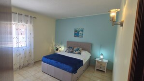 A bedroom with a bed, nightstand, and wall art. - Apartment with Pool & Garden – 200m from Beach – Perfect for Families & Couples (Albufeira)