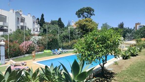 A swimming pool surrounded by greenery, a person walking, and buildings in the background. - Apartment with Pool & Garden – 200m from Beach – Perfect for Families & Couples (Albufeira)