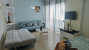 A living room with a sofa, ottoman, coffee table, TV, and a desk with a chair. - Apartment with Pool & Garden – 200m from Beach – Perfect for Families & Couples (Albufeira)