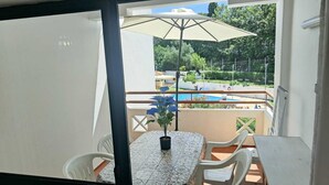 A balcony with a table, chairs, a potted plant, and a pool in the background. - Apartment with Pool & Garden – 200m from Beach – Perfect for Families & Couples (Albufeira)