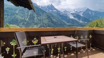 Um deck de madeira com mesa e cadeiras, com vista para uma paisagem montanhosa.