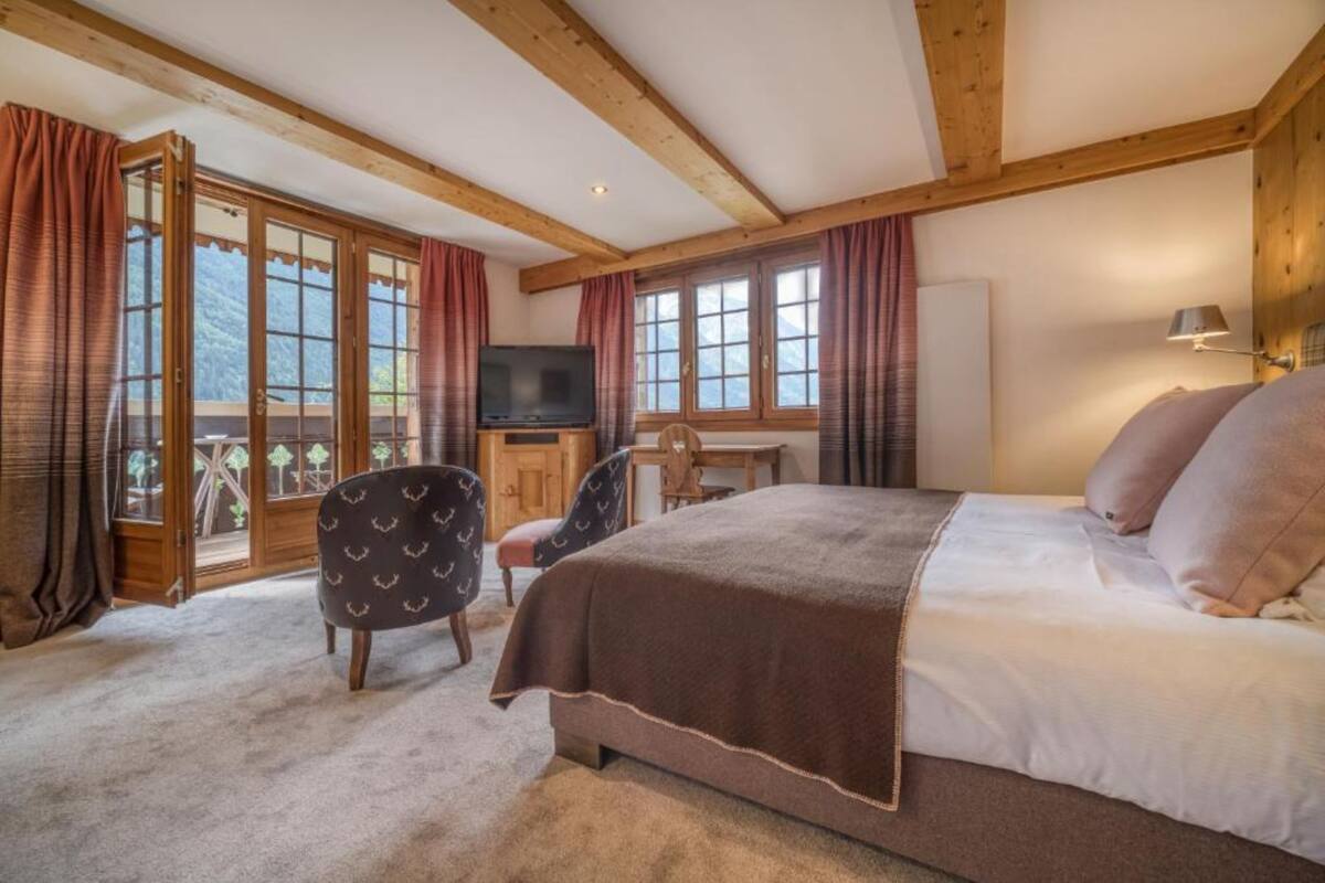 A bedroom with a large bed, wooden beams, a television, a desk, and a chair.
