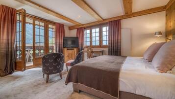 Ein Schlafzimmer mit einem großen Bett, Holzbalken, einem Fernseher, einem Schreibtisch und einem Sessel.