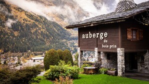 A wooden chalet with a sign reading "auberge du bois princ" surrounded by a lush garden and mountains in the background. - Auberge du Bois Prin (Chamonix-Mont-Blanc)