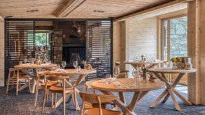 A cozy wooden interior with round tables and chairs, a stone fireplace, and large windows. - Auberge du Bois Prin (Chamonix-Mont-Blanc)