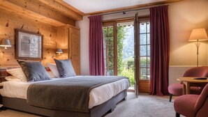A bedroom with a bed, a chair, a table, and a window with curtains. - Auberge du Bois Prin (Chamonix-Mont-Blanc)