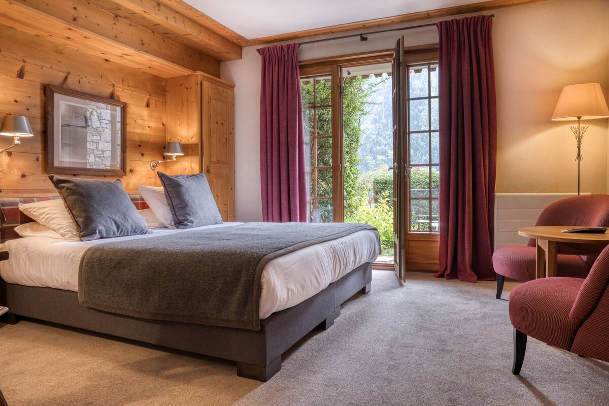 A bedroom with a bed, a chair, a table, and a window with curtains.